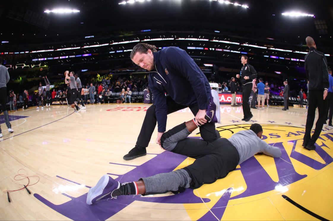 A coach warming up a professional basketball player on court before a game